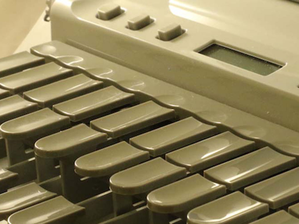 Close-up view of a stenotype machine, showing several dark grey keys and part of a digital display panel, used for court reporting or transcription.