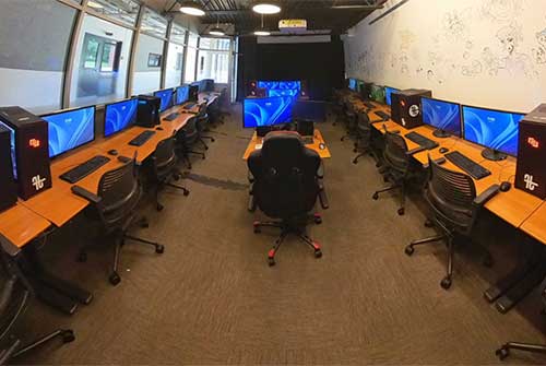 Empty computer lab for undergraduate students, with rows of desks, chairs, monitors, and wall art in a well-lit room.