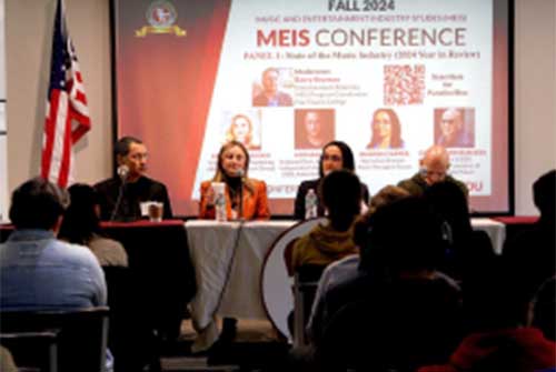 Four undergraduate panelists sit at a table speaking to an audience during the 2024 MEIS Conference, screen behind them.
