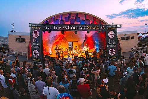 Outdoor concert at sunset as undergraduates enjoy a band on the Five Towns College Stage near the beach.